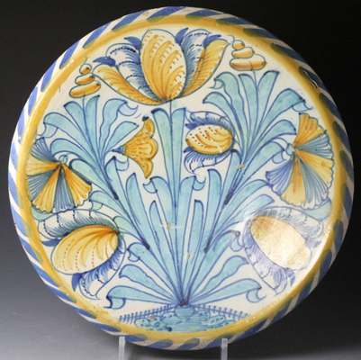 Antique English delftware charger painted with blue and yellow tulips and turquoise leaves inside a blue-dash rim.