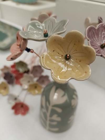 Glazed ceramic flowers on copper wire stems in a sage-green bud vase, by Lucy Ormsby