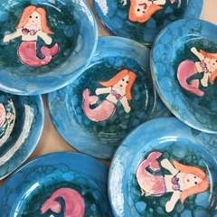 Blue bubble-glazed plates, each painted with an orange-haired mermaid