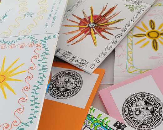 Hand-decorated cards with sunbursts, wave borders and leafy vines, spread across a table
