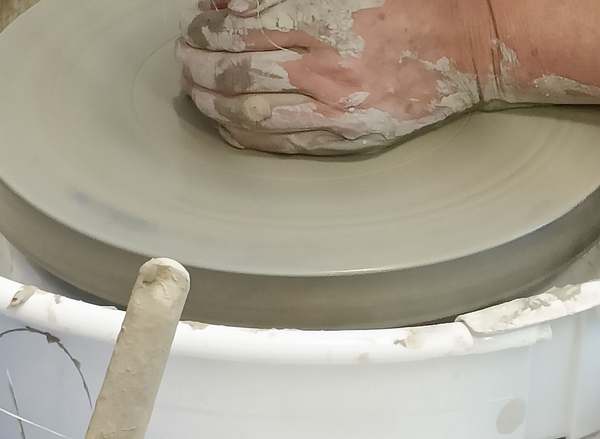 Clay-covered hands shaping clay on a pottery wheel